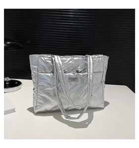 Detailed view of silver quilted tote bag with black logo label on metallic fabric