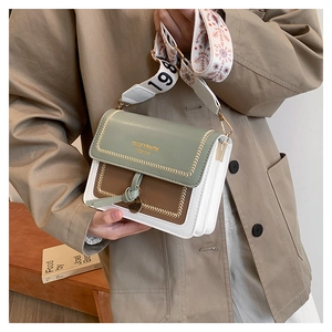 Detail of green and brown square crossbody bag with embroidered wide strap and golden hardware