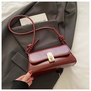 Detail of burgundy leather shoulder bag with gold metal buckle and knotted strap on blazer