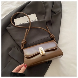 Detail of a brown leather shoulder bag featuring a gold metal lock and knotted strap