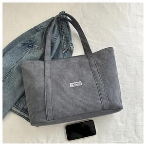 Flat lay of a grey corduroy tote bag with a white fashion label on a textured background