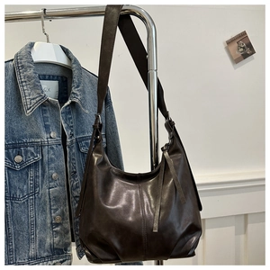 Dunkelbraune Hobo-Tasche aus weichem Kunstleder hängt neben einer Denim-Jacke