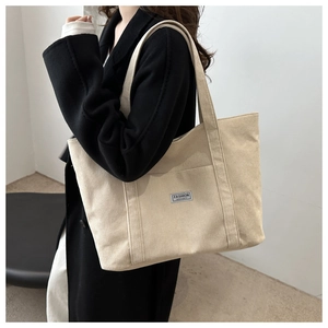 Detail of beige corduroy tote bag with Fashion Instinct label worn with black coat