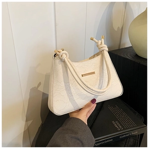 Close-up of white lace shoulder bag with golden metal trim and knotted strap detail
