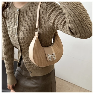 Detail of beige pleated crescent bag with a silver bow clasp held by a model