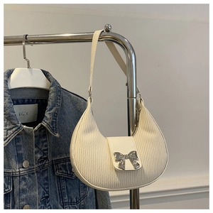 Close-up of a white pleated crescent bag with a silver bow clasp and metallic shoulder strap