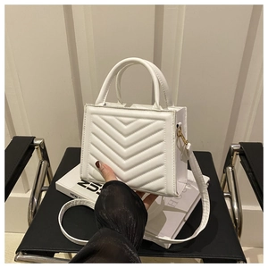 Detailed close-up of white small quilted handbag with V-stitch pattern and gold hardware