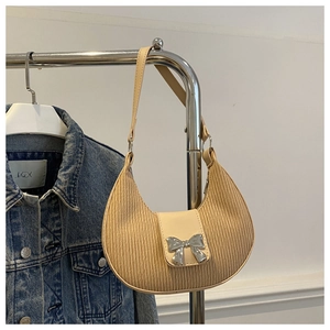 Close-up of beige crescent bag featuring pleated texture and silver bow metal clasp