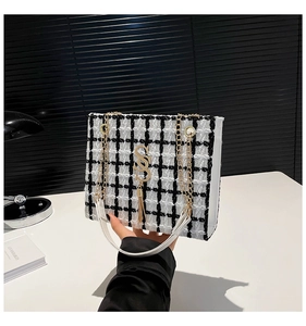 Detail of black and white tweed crossbody bag with golden S-pendant and chain strap