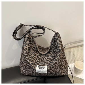 Détail du sac hobo léopard avec étiquette tissée blanche sur un canapé en cuir noir