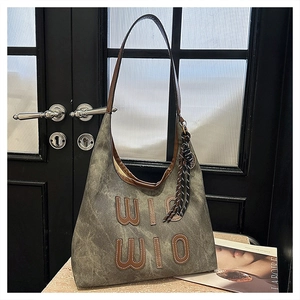 Detail of grey-green canvas tote bag with brown leather WIO letter patch and tassel strap