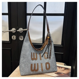 Detail of grey canvas tote bag featuring brown leather WIO applique and woven cord charm