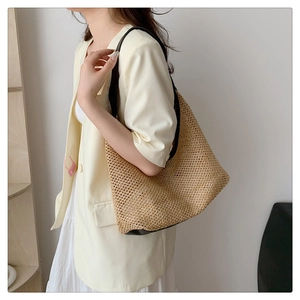 Detail of woven straw tote bag featuring fine texture and slim black leather shoulder straps