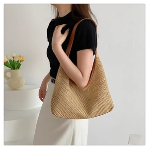 Detail of woven straw tote bag with brown leather shoulder straps on a model
