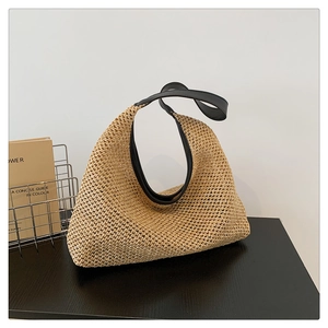 Detail of a beige woven straw tote bag with black leather straps on a modern stand