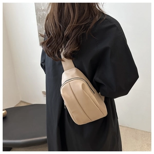 Detail view of a beige minimalist chest bag with black zipper on a model for daily use