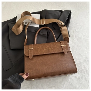 Détail du sac vintage marron avec boucle en métal et large bandoulière sur un blazer