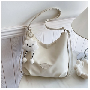 Detail view of a cream crescent underarm bag with a cute white cloud plush pendant charm