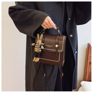 Detail of dark brown leather backpack with embossed text and knit rabbit charm