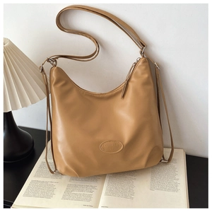 Detail of ginger brown leather tote bag with embossed logo on an open book