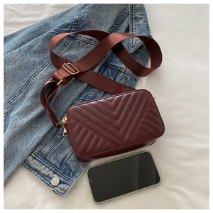 Macro detail of wine red quilted leather camera bag with wide nylon strap on denim