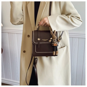 Detail of dark brown leather handbag with white stitching and cute rabbit doll charm