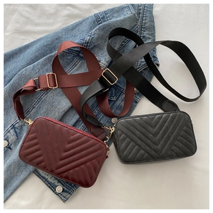 Detail of burgundy and black quilted crossbody bags with wide straps on denim fabric