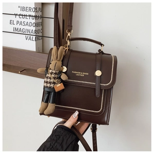 Detail of dark brown leather handbag with white beaded stitching and rabbit charm