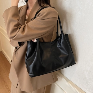 Minimalist black leather tote bag for women shown as a soft shoulder bag on model