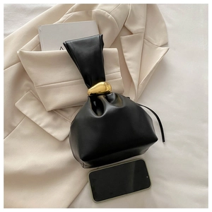 Détail du sac seau noir mat avec boucle dorée emblématique sur un blazer beige