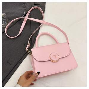 Detailed view of a pink matte leather crossbody bag with a round gold buckle closure