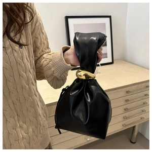 Détail d'un sac seau en cuir noir avec un ornement en métal doré en forme d'olive sur l'anse