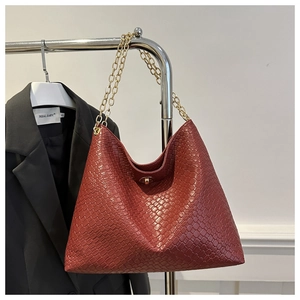 Detail of rust red woven tote bag featuring gold twist lock and metallic chain straps