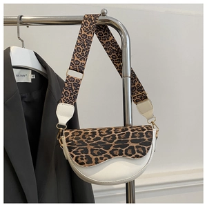 Detail of leopard print saddle bag with wide strap hanging next to a grey blazer