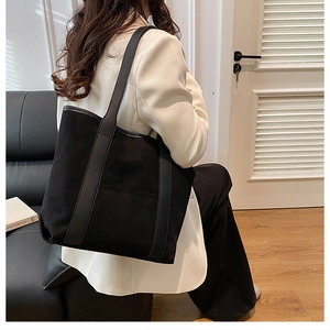 Detailed view of the large black suede tote bag with textured wide leather strap on a model