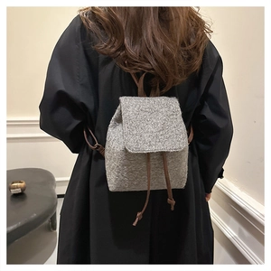 Sac à dos gris en laine avec cordons en cuir marron porté sur le dos, design minimaliste chic