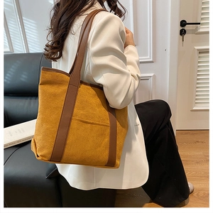 Detail of a large yellow suede tote bag with brown leather straps held by a model