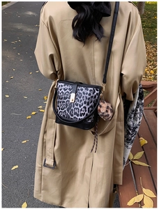 Detail of leopard print bucket bag with plush charm on a tan trench coat backdrop