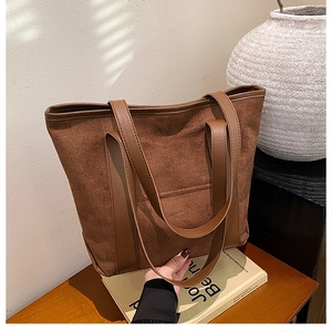 Detail view of large dark brown suede tote bag with wide leather handles on books