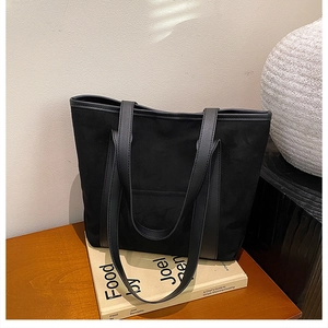 Detail of a black suede tote bag with leather straps resting on a book on a wooden desk