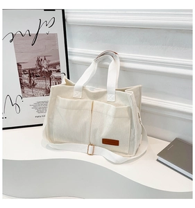 Detail of white corduroy tote bag featuring front pockets and brown fashion logo label