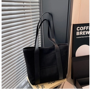 Detail of minimalist black suede tote bag with leather straps on books in grey scene