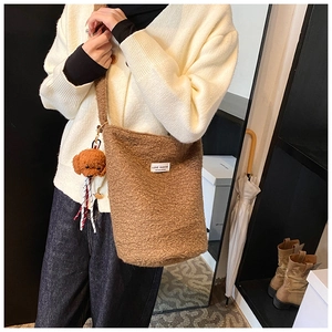 Close-up of brown wool bucket bag with plush bear charm and white woven label detail
