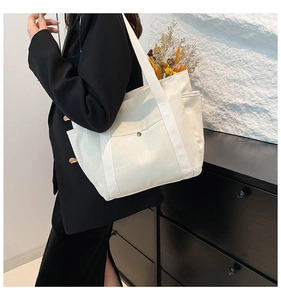 Detail of white canvas tote bag featuring functional side pockets and button front pocket