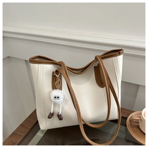 Detail view of cream and brown tote bag with contrast stitching and furry monster charm