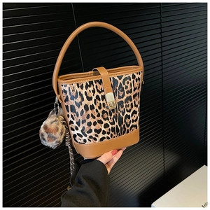Detail of leopard print bucket bag with brown leather trim and plush pom-pom charm