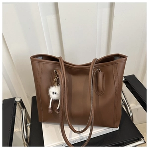 Detail of a brown tote bag with a white plush charm on a modern chair with white books