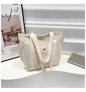 Detail of beige canvas tote bag with side pockets and front metal buckle on a white stand