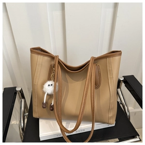 Detail of khaki tote bag with contrast stitching and plush monster charm on leather chair