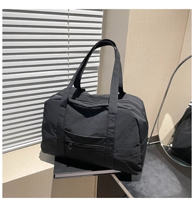 Detailed macro view of black nylon tote bag with reinforced handles and front zipper pocket